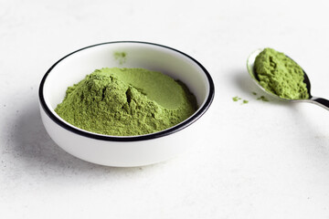 Green superfood powder in white bowl. Powder mix from wheat grass, barley grass, chlorella, spirulina, maca, matcha. healthy supplement to improve health. close-up. selective focus