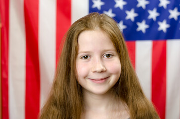 The red-haired girl looks at the camera and smiles. Girl on the background of the flag of America