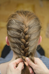 A woman braids a pigtail for a red-haired girl. Hair weaving hairstyles. Braiding close up