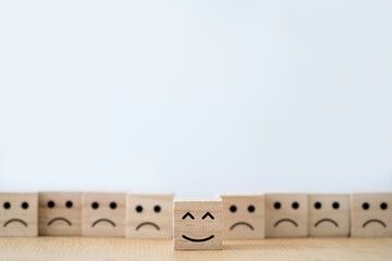 Smile face print screen on wooden block cube in front of sadness face.
