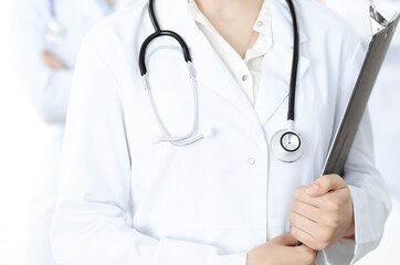 Unknown woman-doctor standing straight with clipboard of medication history record in clinic, close-up. Medicine concept