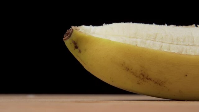 Macro shot of Peeling a ripe banana on a black background on a wooden cutting board.