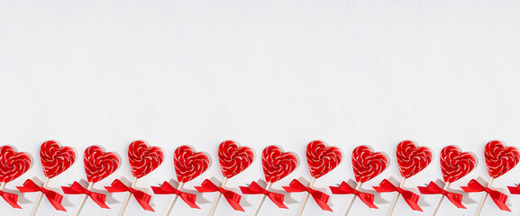 Fun valentine's day background - sweet red lollipops hearts with bows on white wood board as decorative seamless border for banner, header, overhead, copy space.