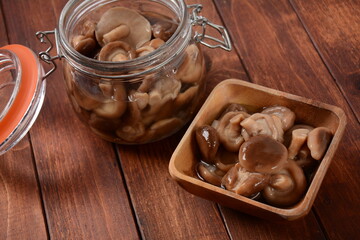Glass jar and wooden bowl with homemade pickled forest mushrooms honey agarics,  on old wooden board . Fermented healthy food.