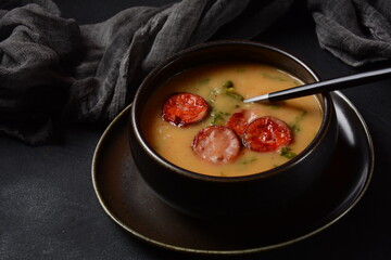 Caldo Verde Soup with greens and chopped chorizo on the top in the bowl on a dark background.