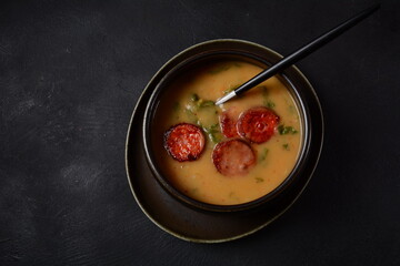 Caldo Verde Soup with greens and chopped chorizo on the top in the bowl on a dark background.