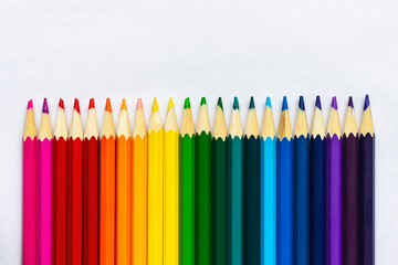 Colored pencils lying in a row on a sheet of white paper.