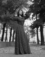 Elegant caucasian brunette woman with long wavy hair in long brown dress with floral print walking at tree alley with colorful foliage