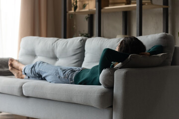 Obraz premium Back view of calm young Caucasian woman lying relaxing on sofa in living room relieve negative emotions. Millennial rest on couch at home dreaming and sleeping on weekend. Stress free concept.