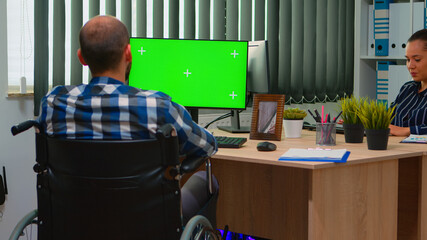 Handicapped disabled freelancer looking at pc with green screen talking with colleagues. Immobilized businessman in wheelchair using computer with chroma key, mockup, greenscreen for videomeeting.