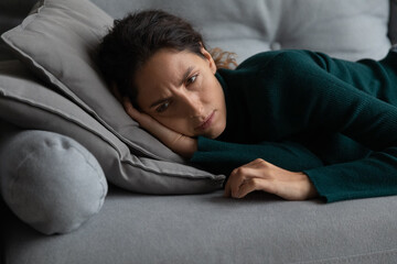 Upset millennial Caucasian woman lying on sofa missing feeling lonely abandoned at home. Unhappy...