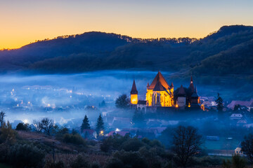Biertan, Romania. Foggy sunset at the saxon village with the fortified church, Transylvania. - obrazy, fototapety, plakaty