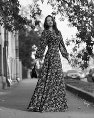 Elegant caucasian brunette woman with long wavy hair in long colorful dress with floral print...