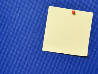Yellow paper note with pin board over blue background.Copy space.