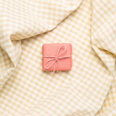 Pink gift box on crumpled beige check pattern fabric background. top view