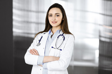 Young smiling woman-doctor is standing with arms crossed in a clinic office. Portrait of a friendly physician woman. Perfect medical service in a hospital. Medicine concept