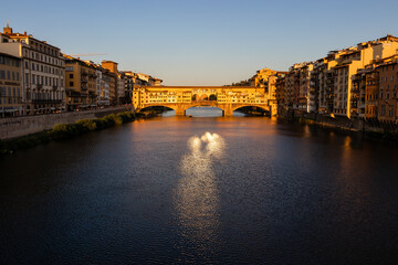 view of the famous Ponte Vecchio bridge over the Arno river and the hiding houses before sunset.