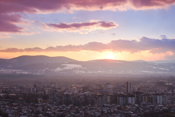 Blue hour view of Pirot cityscape on a cold, frosty, winter day with snow on the houses and distant horizon mountains under colorful sky