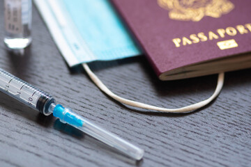 Syringe with needle, vial, surgical face mask and passport or visa on a white table ready to be...
