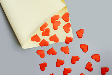 Red hearts fly from yellow package on a gray background. Copy space. Flat lay.