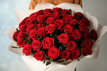 Woman holding luxury bouquet of fresh red roses on light background, closeup © New Africa