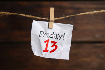 Crumpled paper note with phrase Friday! 13 hanging on twine against wooden background. Bad luck...