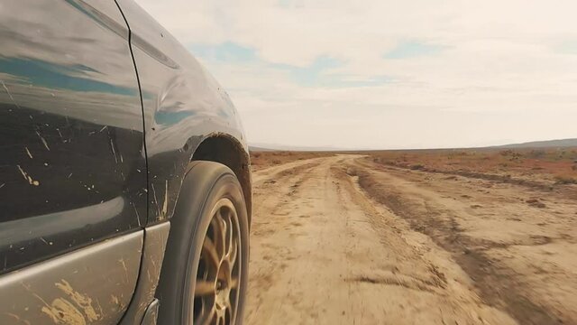 Super slow motion front 4WD wheel spin on dusty gravel road in scenic location.