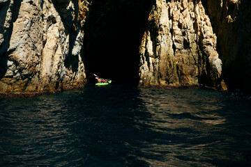 Selective focus - father and son rowing in a canoe to enter a natural cave in the Mediterranean Sea