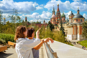 Tourists in Moscow look at St. Basil's Cathedral. The woman shows in the direction of the Kremlin and red square. Tourist in Russia in summer, green grass, Sunny day, cloudy sky