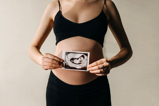 Pregnant woman holding baby ultrasound image in front of her belly.