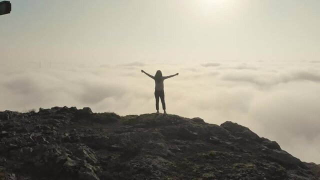 Inspirational aerial view around victorious young attractive woman with spread hands above the clouds. Daydreaming concept