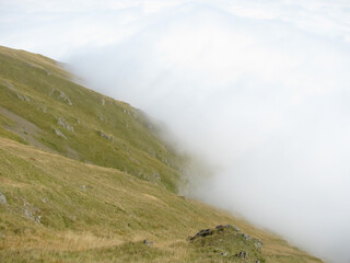 Fototapeta na wymiar Russia, North Ossetia. The road to the Fiagdon relay. The green slope of the mountain and the white clouds advancing below the level of the mountains.