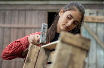 Caucasian woman carpenter knocks on a wooden box with a hammer. Young feminist girl worker hammers nails. Gender equality concept