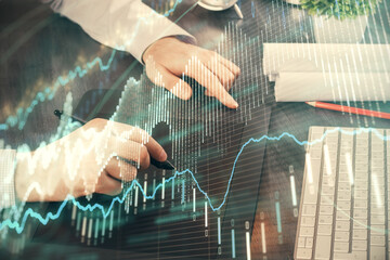 Double exposure of man's hands holding and using a phone and financial graph drawing. Analysis concept.