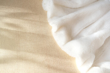 White delicate soft background of plush fabric folds on light golden background with shadow and sunlight. Copy space. Flat lay. Details of warm winter clothes