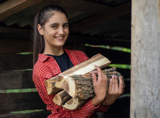 Young Caucasian girl holding firewood for the fireplace. Country woman picks firewood and smiles