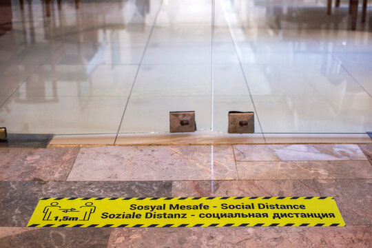 Yellow sign on marble floor in front of the glass door, with inscription Social distance 1,5m in Russian, English and Turkish