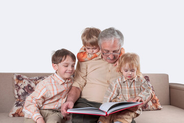 Positive elderly man reading a book for his three little grandchildren (friendly family concept)