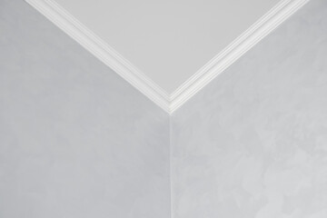 White ceiling with a white plinth in a room with gray painted walls. Decoration of the corner between the ceiling and the wall in the room. Ceiling molding in the interior. Detail of corner.