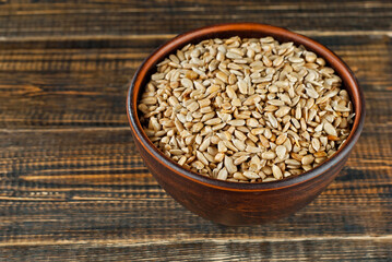 Sunflower seeds in a clay bowl on an old shabby board. Nuts on a brown wooden table.