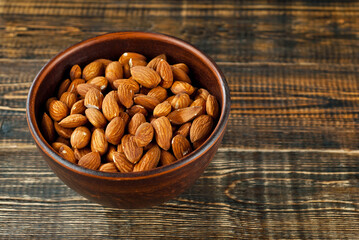 Almonds in a clay bowl on an old shabby board. Nuts on a brown wooden table.