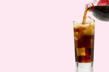 Pouring Cola to glass with ice cubes isolated on pink