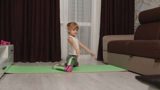 Fit little girl kid doing gymnastics stretching workout at home, watching online lessons on laptop pc. Child pupil online video distance sport exercises education during coronavirus covid-19 lockdown