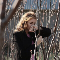 A beautiful girl in a stylish black coat and with a beautiful hairstyle against the background of strict trees. Restraint and style.