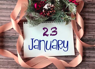 January 23 on a white Notepad.Nearby fir branches, red berries, cones and a ribbon on a wooden background.