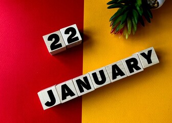 January 22 in black letters on wooden blocks on a divided yellow-red background .Next to a flower...