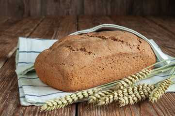Freshly baked bread with a kitchen towel and ears on a rustic wooden background. Healthy food. Concept of homemade bread