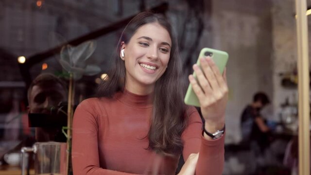 Smiling businesswoman using smartphone and wireless handsfree for online meeting, video call, video conference. Communication online with colleagues,relatives,friends. Online education,remote working