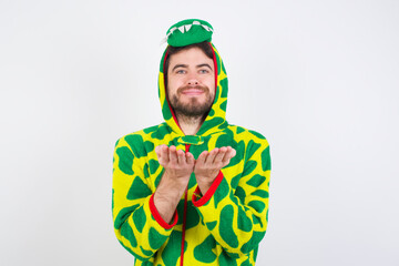 Young caucasian man wearing a pajama standing against white background holding something with open palms, offering to the camera.