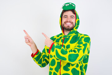 Fototapeta premium Young caucasian man wearing a pajama standing against white background indicating finger empty space showing best low prices, looking at the camera
